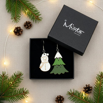 Snowman and Christmas tree earrings presented in a gift box with pine branches, pinecones, and warm fairy lights, creating a festive holiday atmosphere. Handmade in Finland by byMinta.