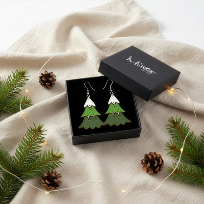 Christmas tree earrings presented in a gift box with pine branches, pinecones, and soft fairy lights, creating a festive holiday atmosphere. Handmade in Finland by byMinta.