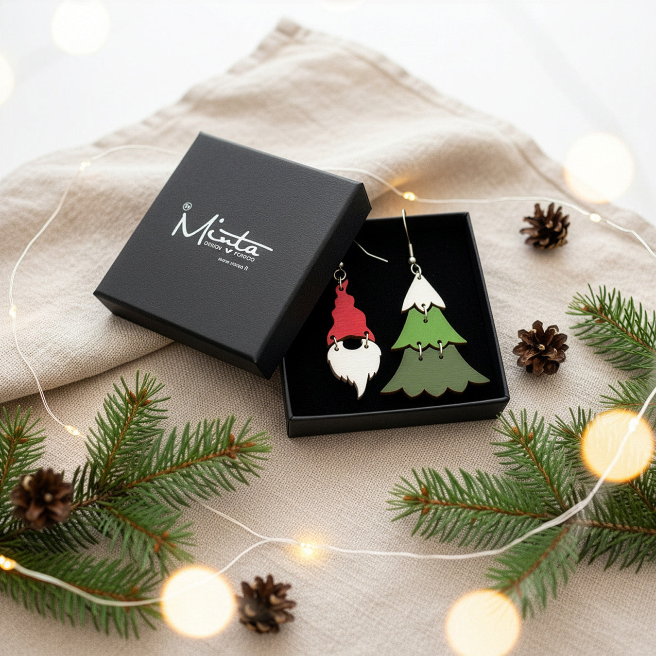Gnome and Christmas tree earrings presented in a gift box with pine branches, pinecones, and warm fairy lights in a festive holiday setting. Handmade in Finland by byMinta.