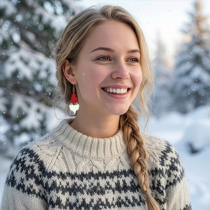 Smiling blonde woman wearing red and white Christmas gnome earrings in a snowy winter landscape, dressed in a traditional Nordic sweater. Handmade in Finland by byMinta.