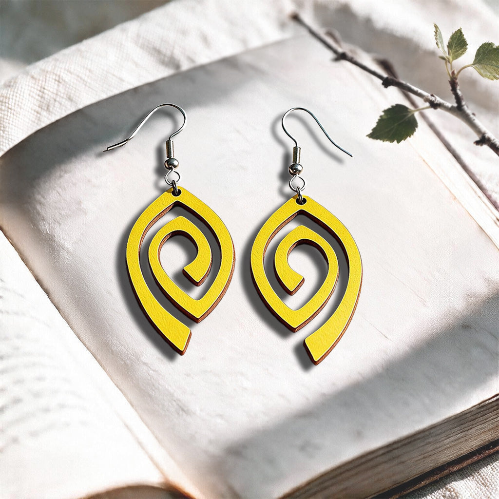 Yellow Labyrinth plywood earrings made in Finland, photographed on a vintage book in natural sunlight