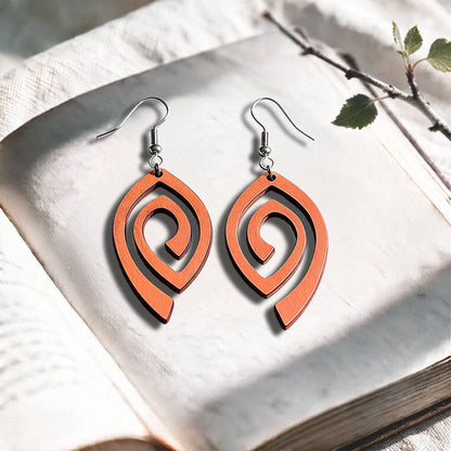 Papaya Labyrinth plywood earrings made in Finland, photographed on a vintage book in natural sunlight