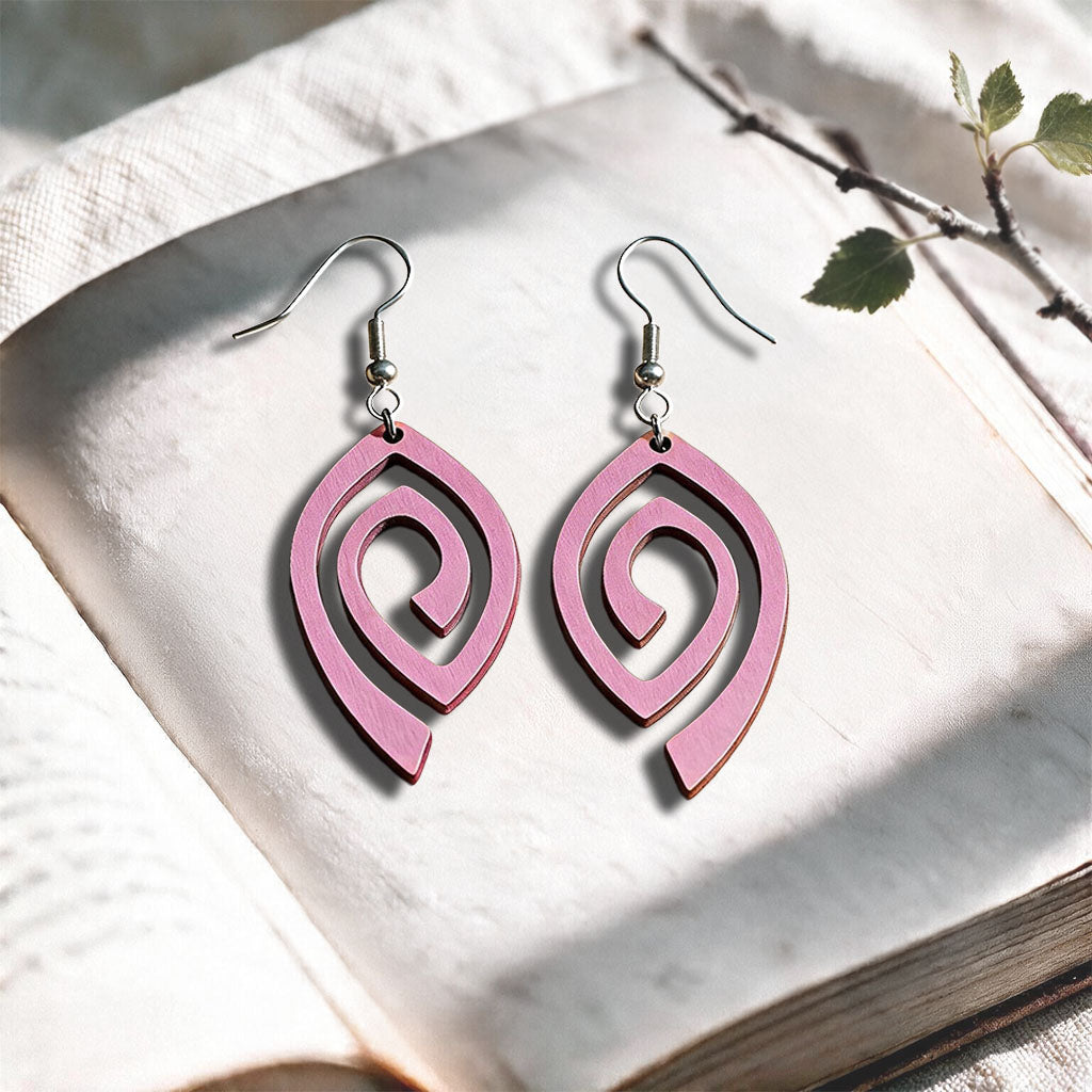 Mauve Labyrinth plywood earrings made in Finland, photographed on a vintage book in natural sunlight