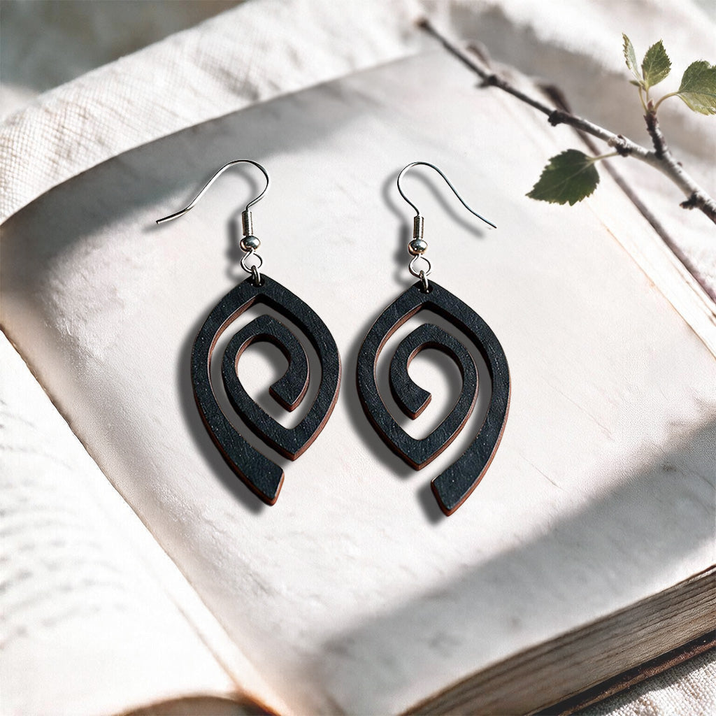 Black Labyrinth plywood earrings made in Finland, photographed on a vintage book in natural sunlight