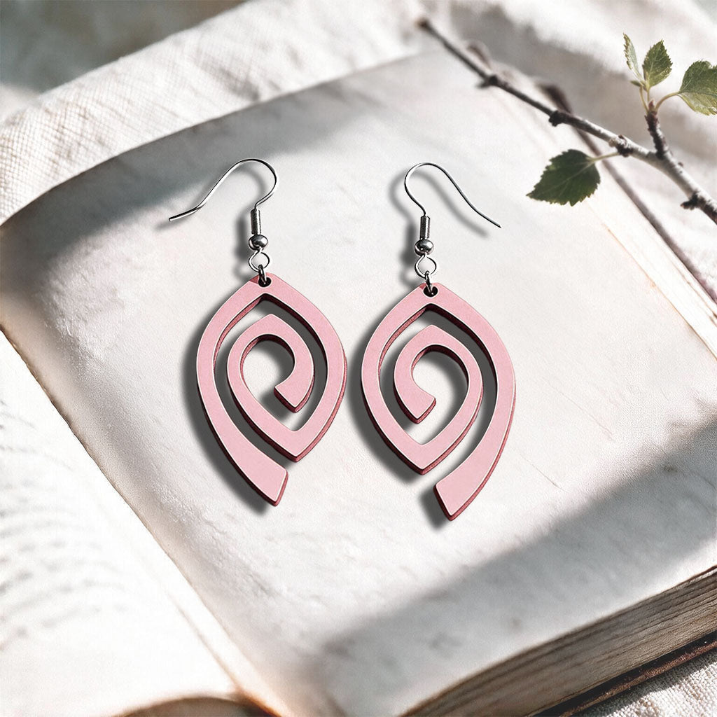Light Pink Labyrinth plywood earrings made in Finland, photographed on a vintage book in natural sunlight