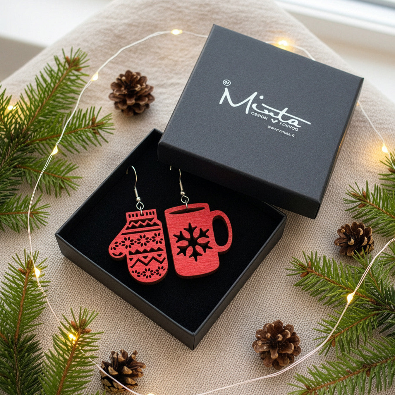 Christmas earrings presented in a gift box with pine branches, pinecones, and warm fairy lights, creating a cozy and festive winter atmosphere. Handmade in Finland by byMinta.