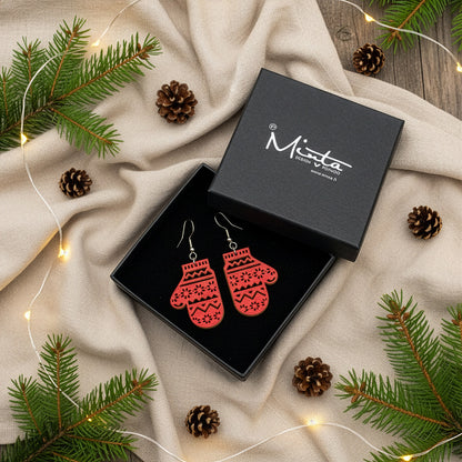 Red mitten earrings presented in a gift box with pine branches, pinecones, and warm fairy lights, creating a festive Christmas atmosphere. Handmade in Finland by byMinta.