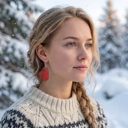 Blonde woman wearing red mitten earrings in a snowy winter landscape, dressed in a traditional Nordic knit sweater. Handmade in Finland by byMinta.
