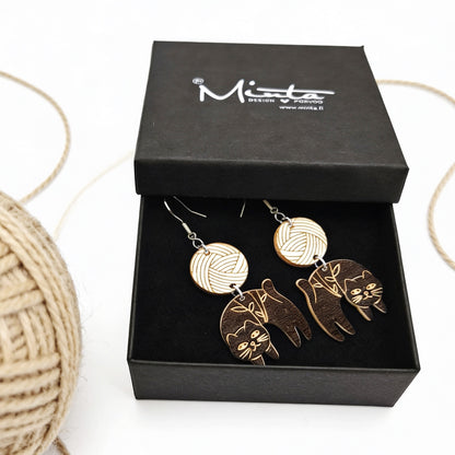 Handmade black cat earrings displayed in a black jewelry gift box beside a ball of natural yarn. Lightweight Finnish birch plywood earrings with engraved cat details, styled in a cozy Nordic craft atmosphere.
