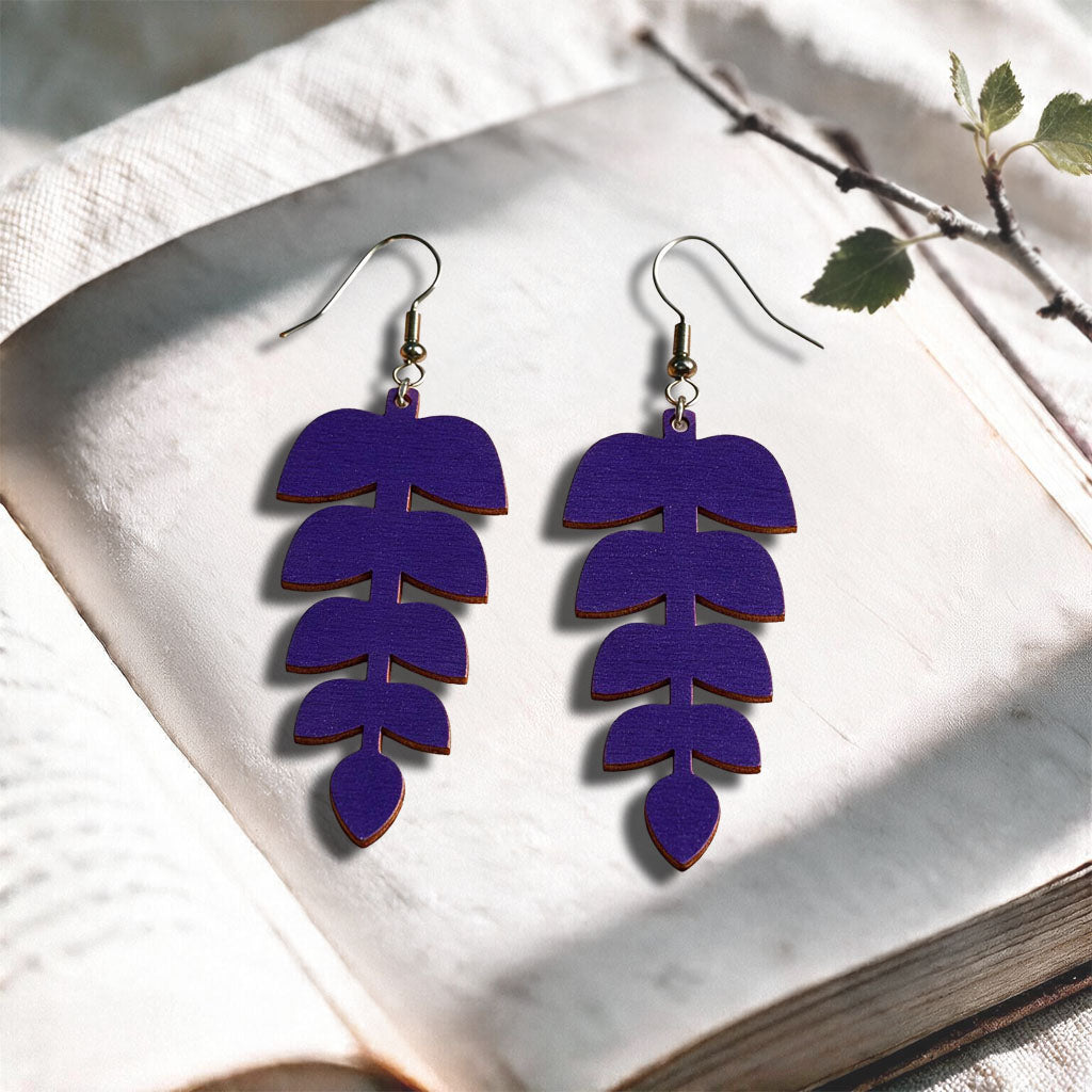 Plum Leaflet plywood earrings made in Finland, photographed on a vintage book in natural sunlight
