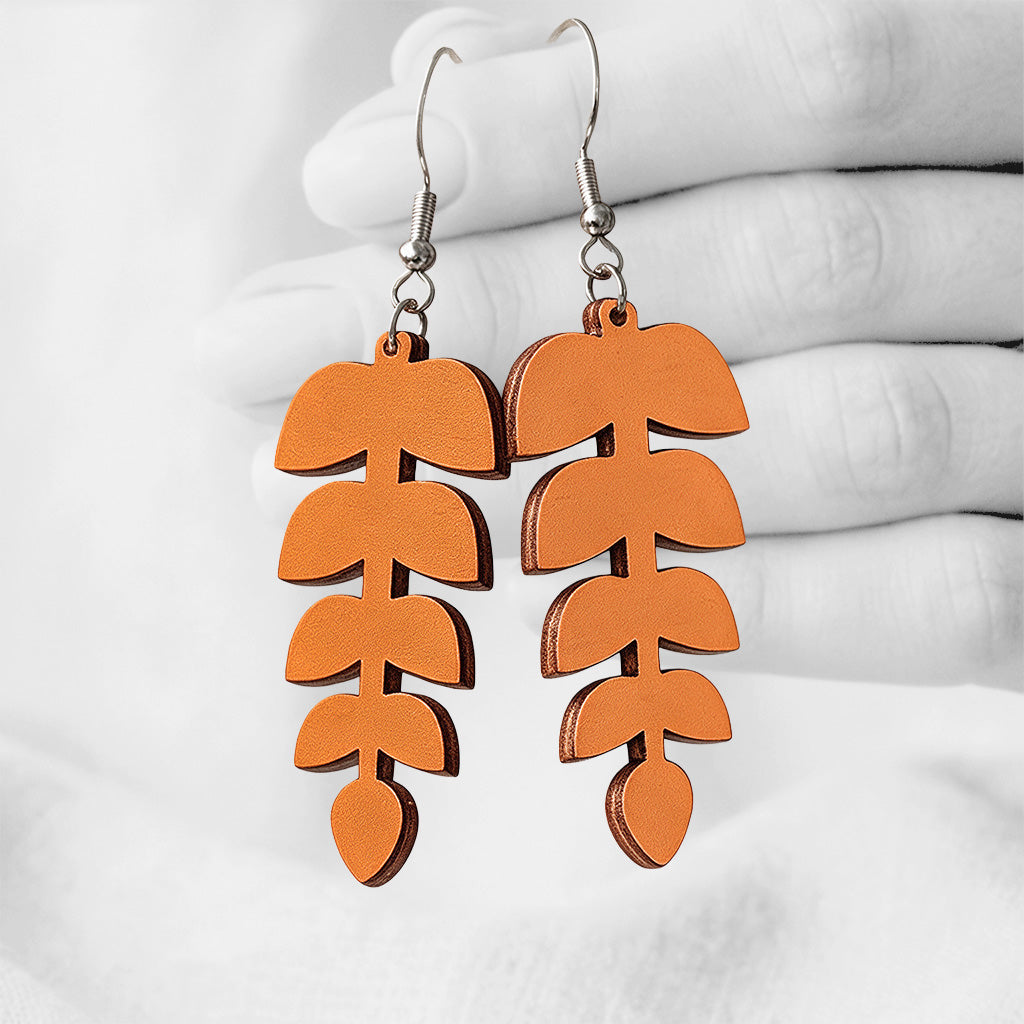Orange Lehdykkä (Leaflet) plywood earrings made in Finland, photographed hanging from a hand in black and white against a softly blurred light background.