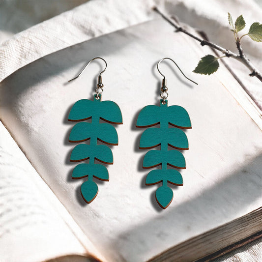 Petrol Leaflet plywood earrings made in Finland, photographed on a vintage book in natural sunlight