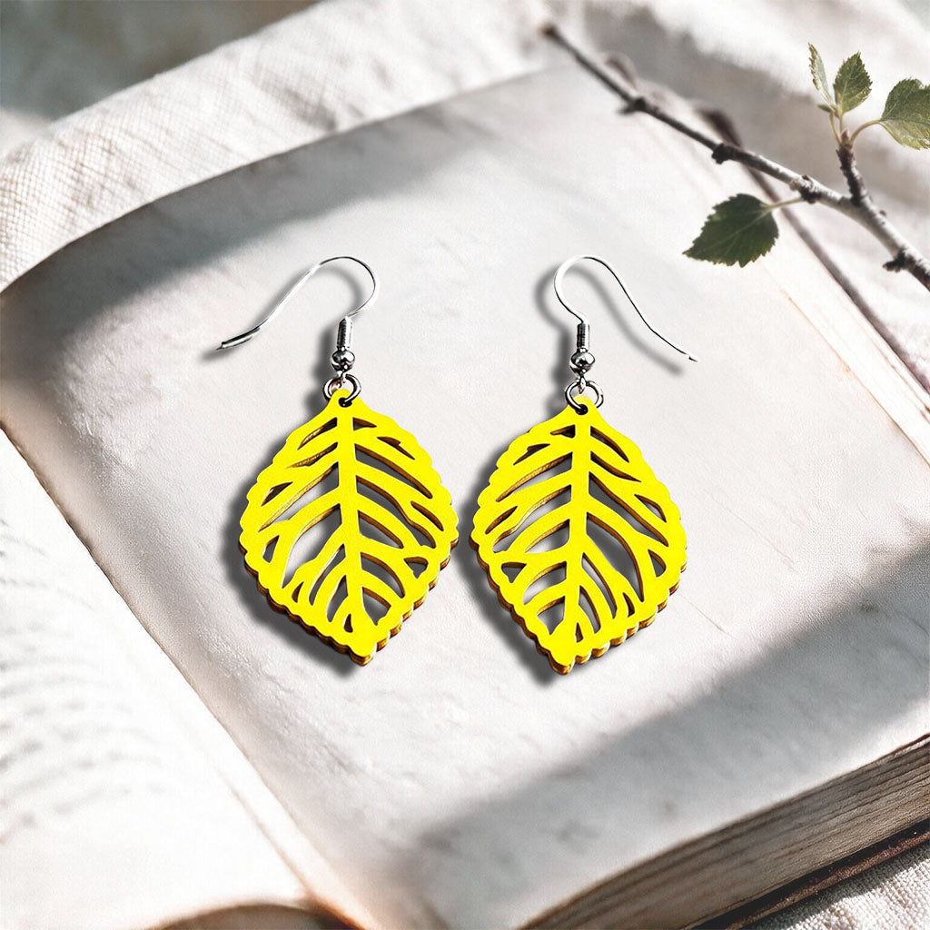 Yellow Leaf plywood earrings made in Finland, photographed on a vintage book in natural sunlight