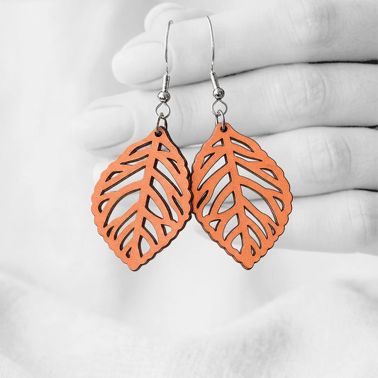 Coral  Lehti (Leaf) plywood earrings handmade in Finland, photographed hanging against a black-and-white hand background.