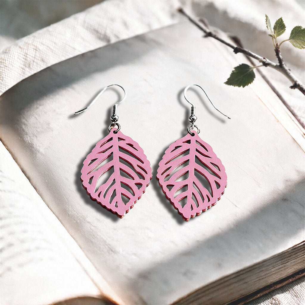 Mauve Leaf plywood earrings made in Finland, photographed on a vintage book in natural sunlight