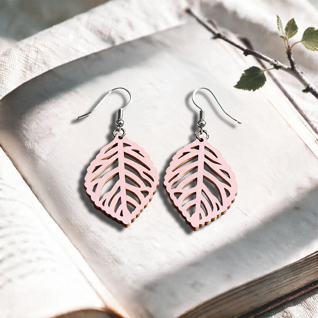 Light pink Leaf plywood earrings made in Finland, photographed on a vintage book in natural sunlight