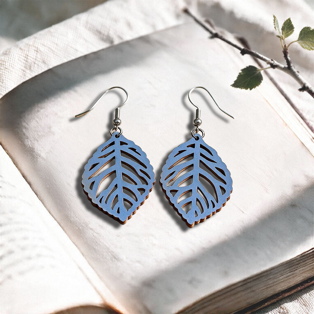 Light blue Leaf plywood earrings made in Finland, photographed on a vintage book in natural sunlight