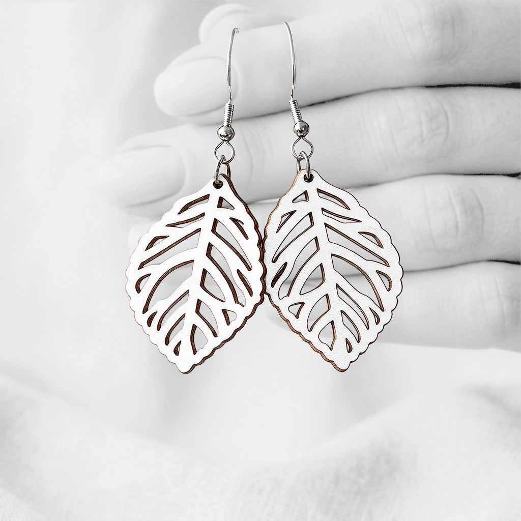 White Lehti (Leaf) plywood earrings handmade in Finland, photographed hanging against a black-and-white hand background.