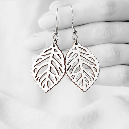 White Lehti (Leaf) plywood earrings handmade in Finland, photographed hanging against a black-and-white hand background.
