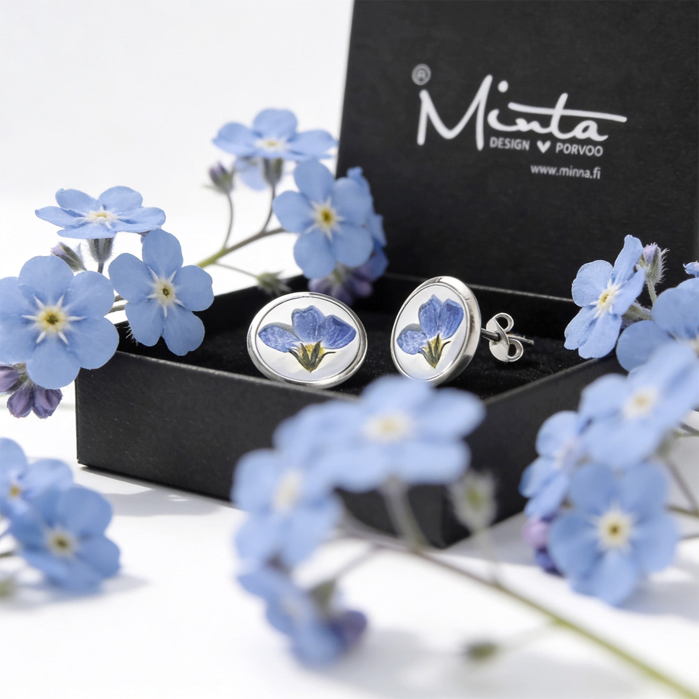 Forget-me-not stud earrings with real blue flowers in a byMinta jewelry box surrounded by delicate blue woodland flowers, handmade in Finland.