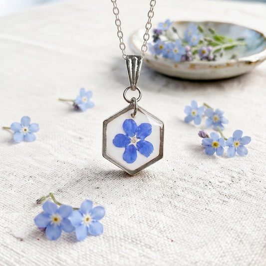 Blue forget-me-not flower preserved in resin hexagon pendant necklace on linen background.