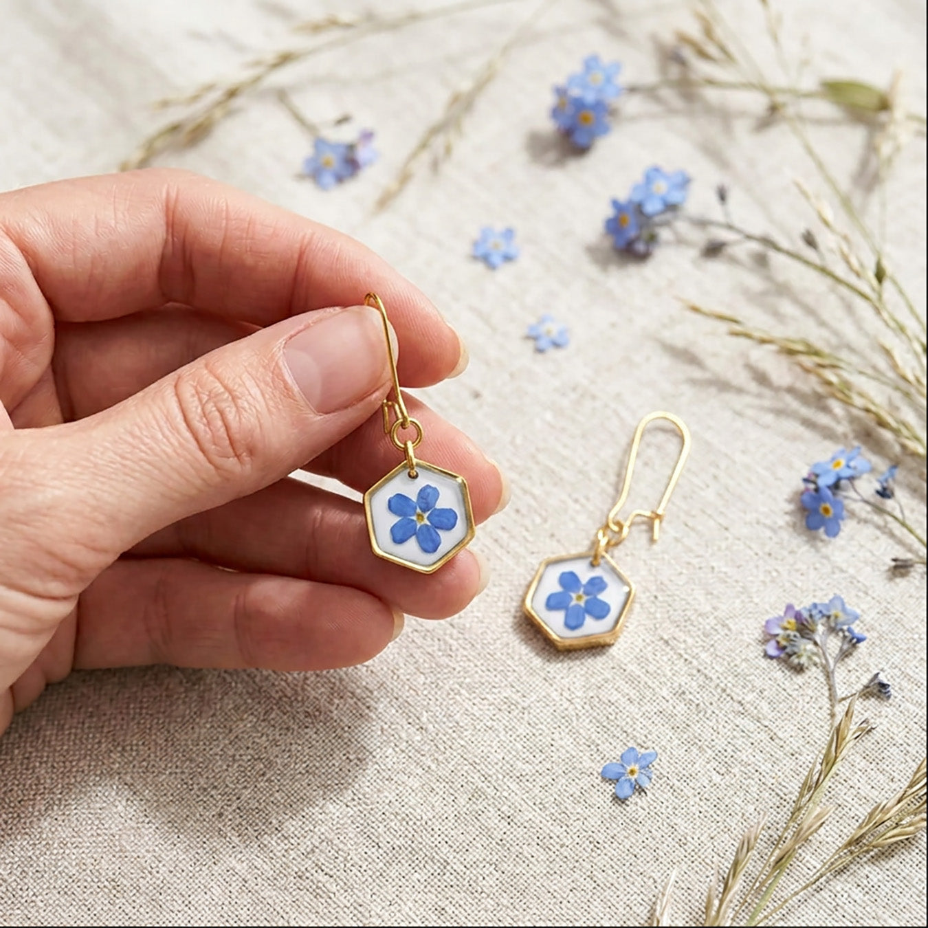 Close-up of handmade forget-me-not earrings with real flowers and 18K gold plated hooks on linen fabric