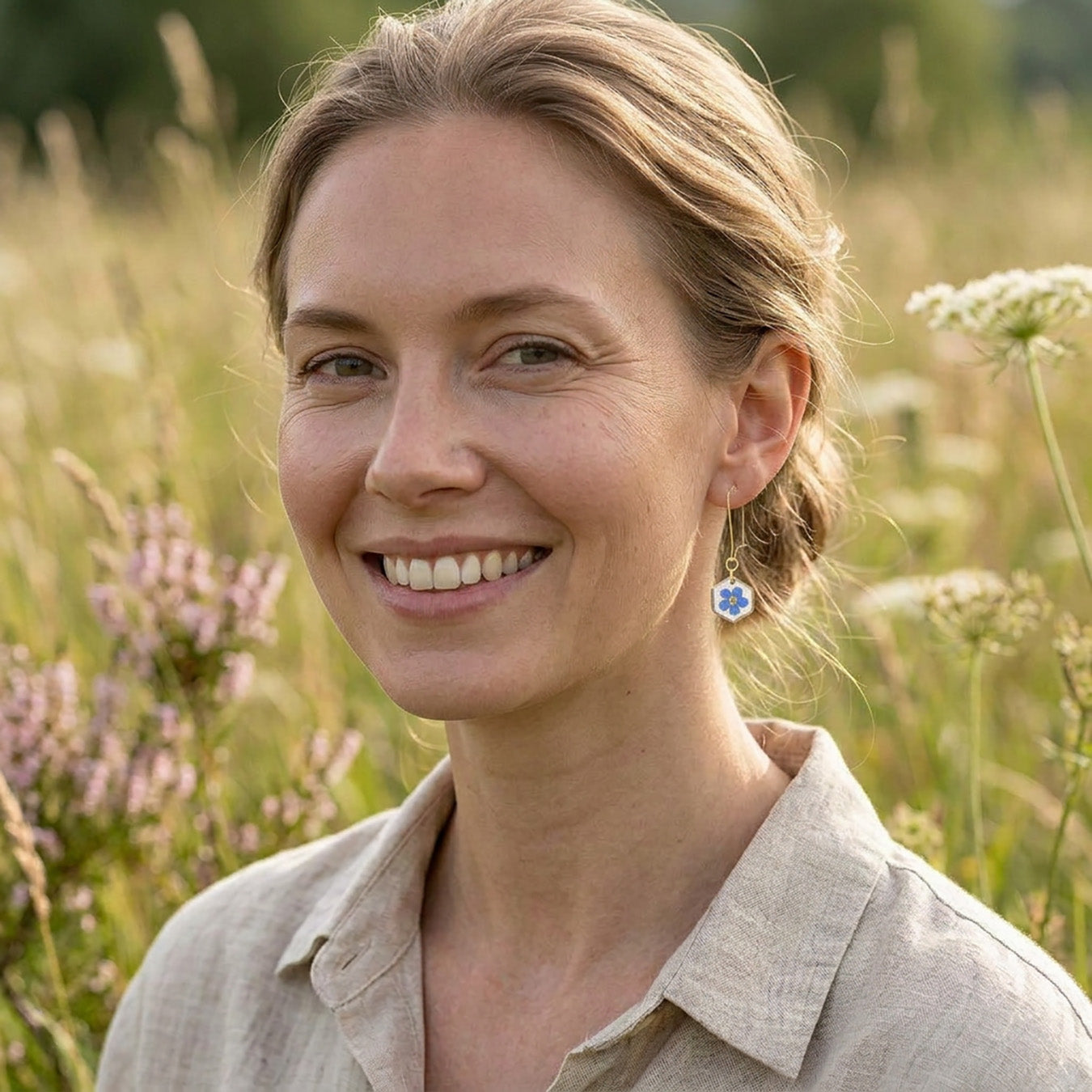 Woman wearing delicate forget-me-not flower earrings with 18K gold plated hooks in a summer meadow