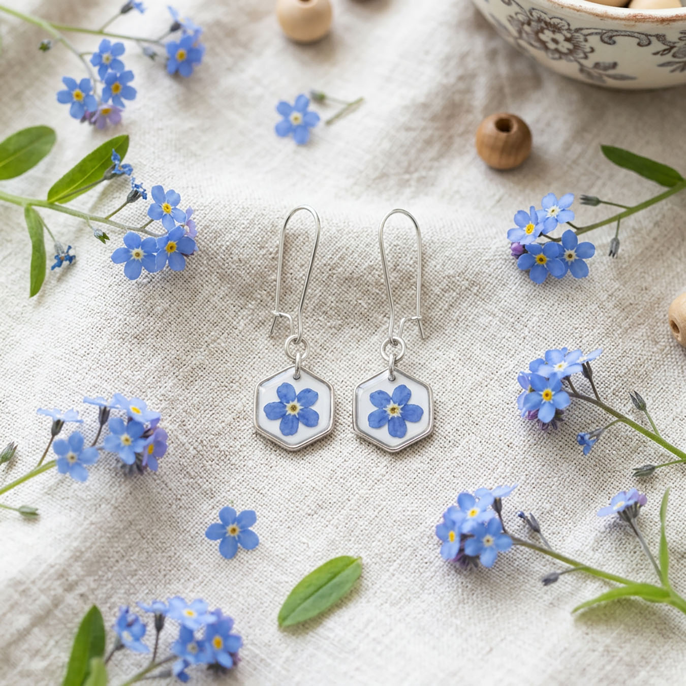 Handmade forget-me-not earrings with real blue flowers displayed on linen with fresh forget-me-nots and greenery