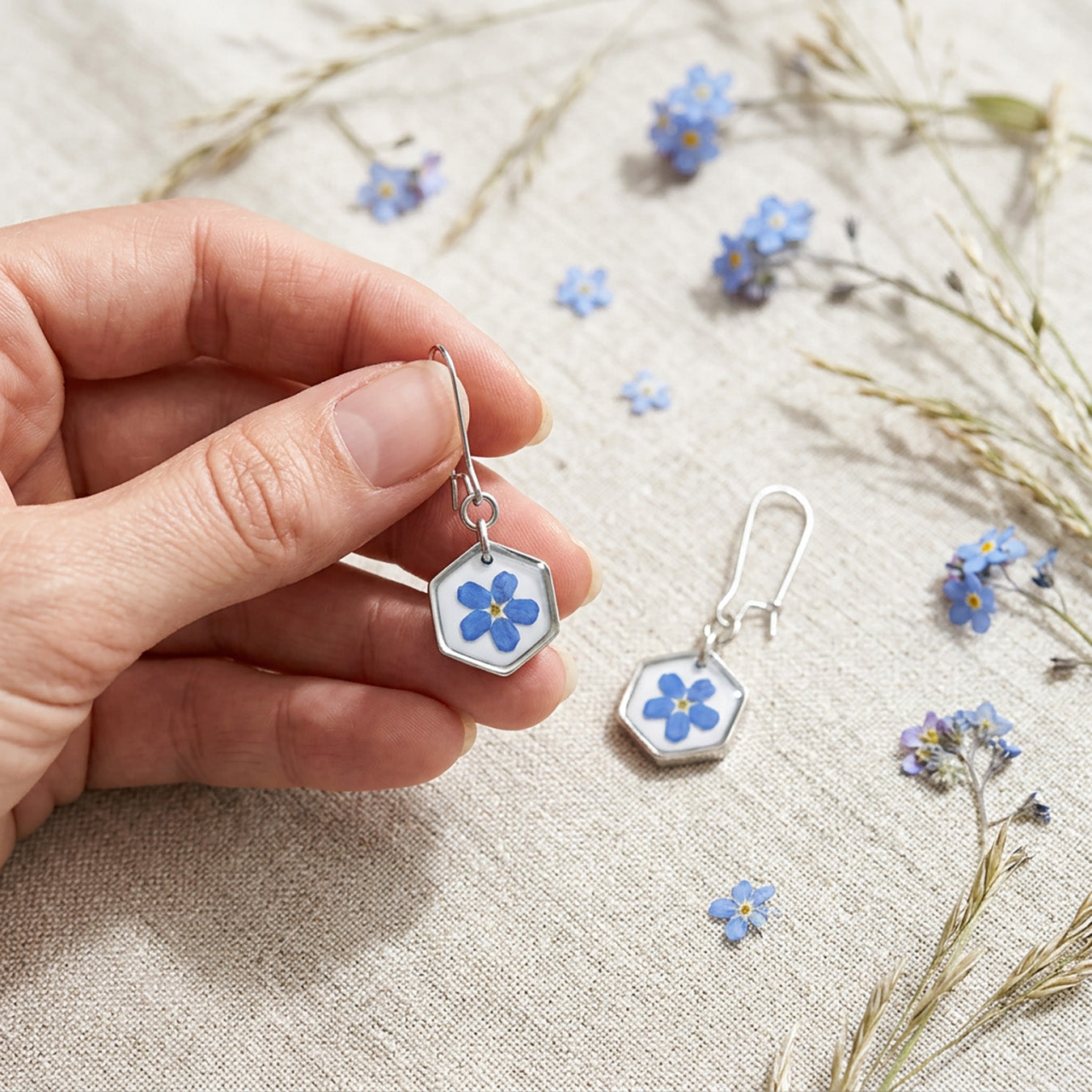 Close-up of handmade forget-me-not flower earrings with real flowers on linen fabric and dried meadow flowers