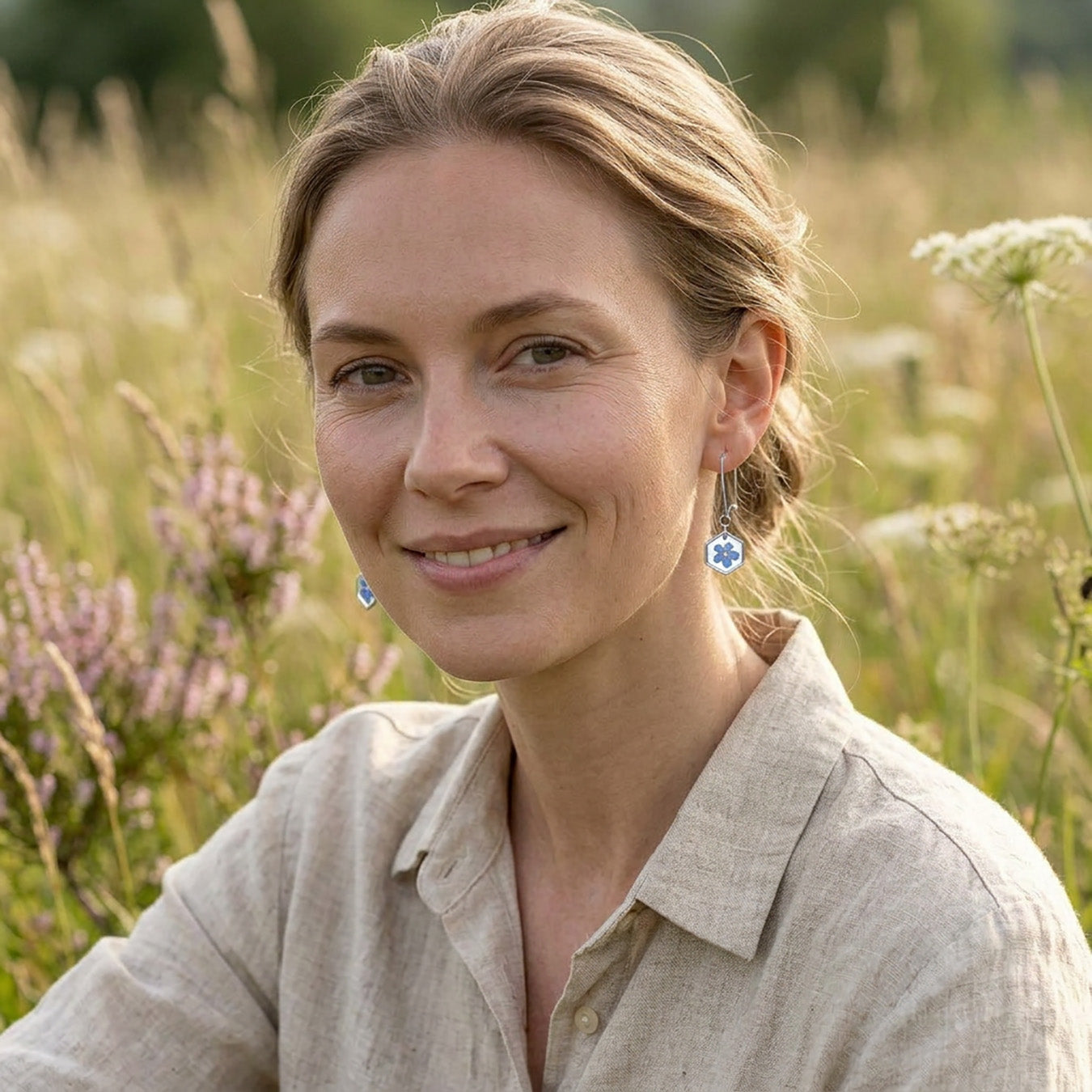 Woman wearing delicate forget-me-not flower earrings in a sunny meadow, handmade botanical jewelry