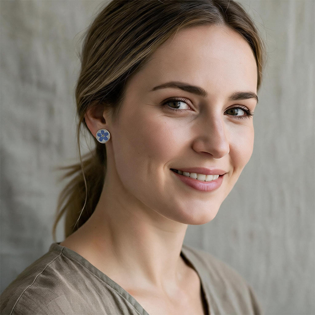 Woman wearing handmade forget-me-not flower earrings with real blue flowers preserved in resin, handcrafted in Finland.
