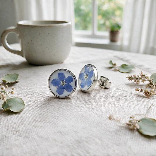 Forget-me-not stud earrings with real blue flowers preserved in resin, photographed on a linen background.
