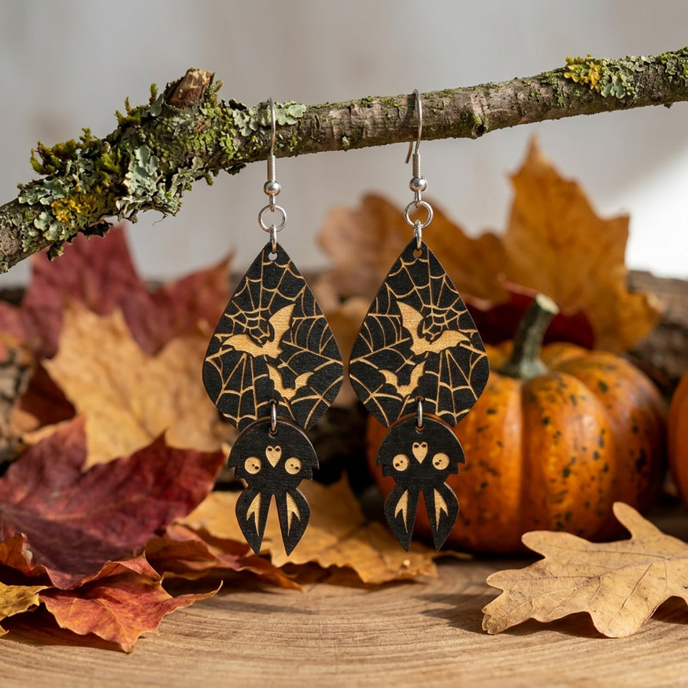 Spider Web Bat Earrings hanging from a moss-covered branch in an autumn setting.