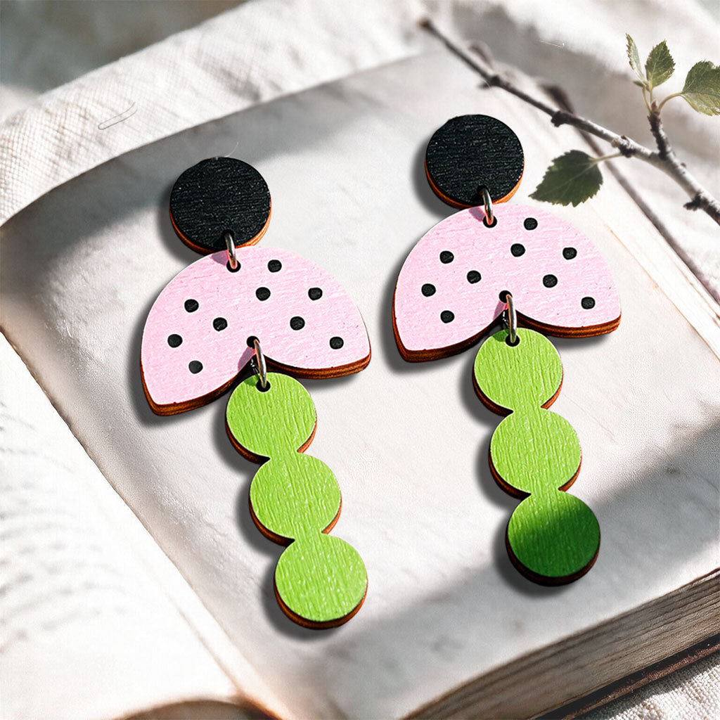 Pink green and black Ladybug stud plywood earrings made in Finland, photographed on a vintage book in natural sunlight