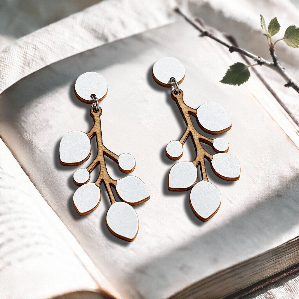 White Snowberry stud plywood earrings made in Finland, photographed on a vintage book in natural sunlight