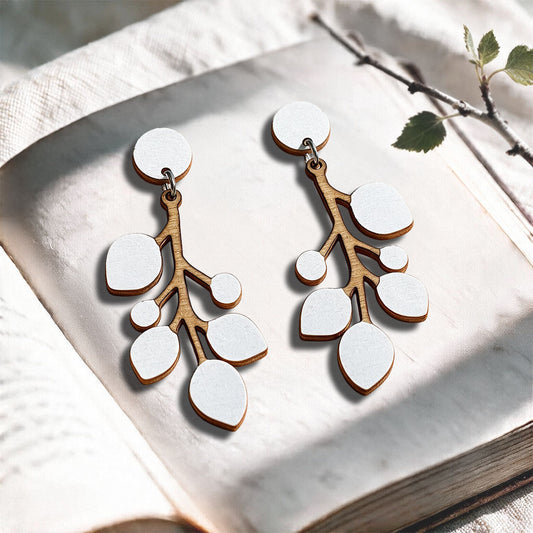 White Snowberry stud plywood earrings made in Finland, photographed on a vintage book in natural sunlight