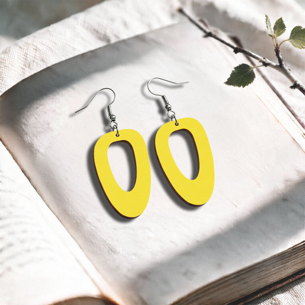 Yellow wood Islet plywood earrings made in Finland, photographed on a vintage book in natural sunlight