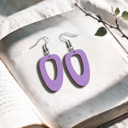 Light violet wood Islet plywood earrings made in Finland, photographed on a vintage book in natural sunlight