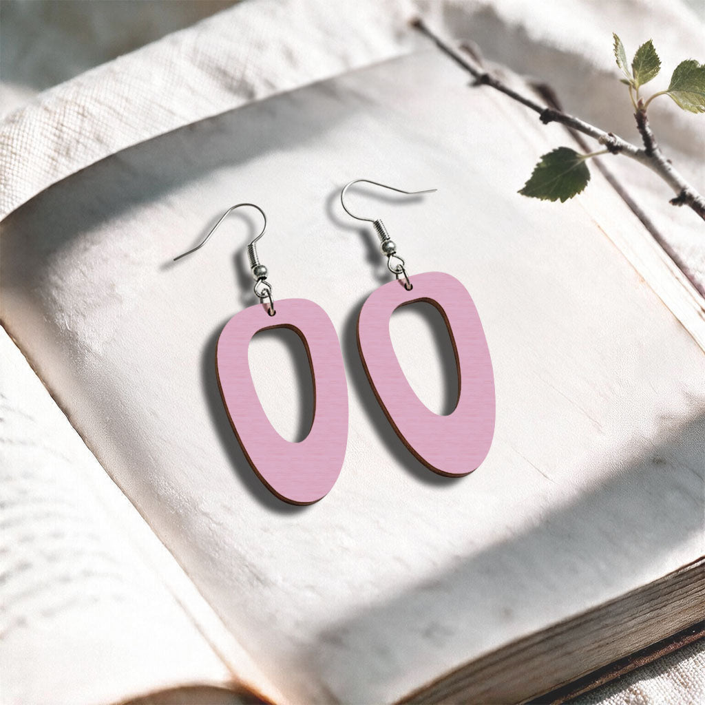 Mauve wood Islet plywood earrings made in Finland, photographed on a vintage book in natural sunlight