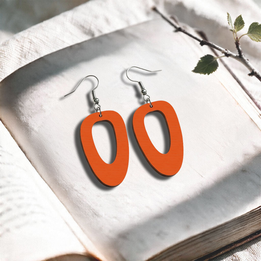 Orange wood Islet plywood earrings made in Finland, photographed on a vintage book in natural sunlight