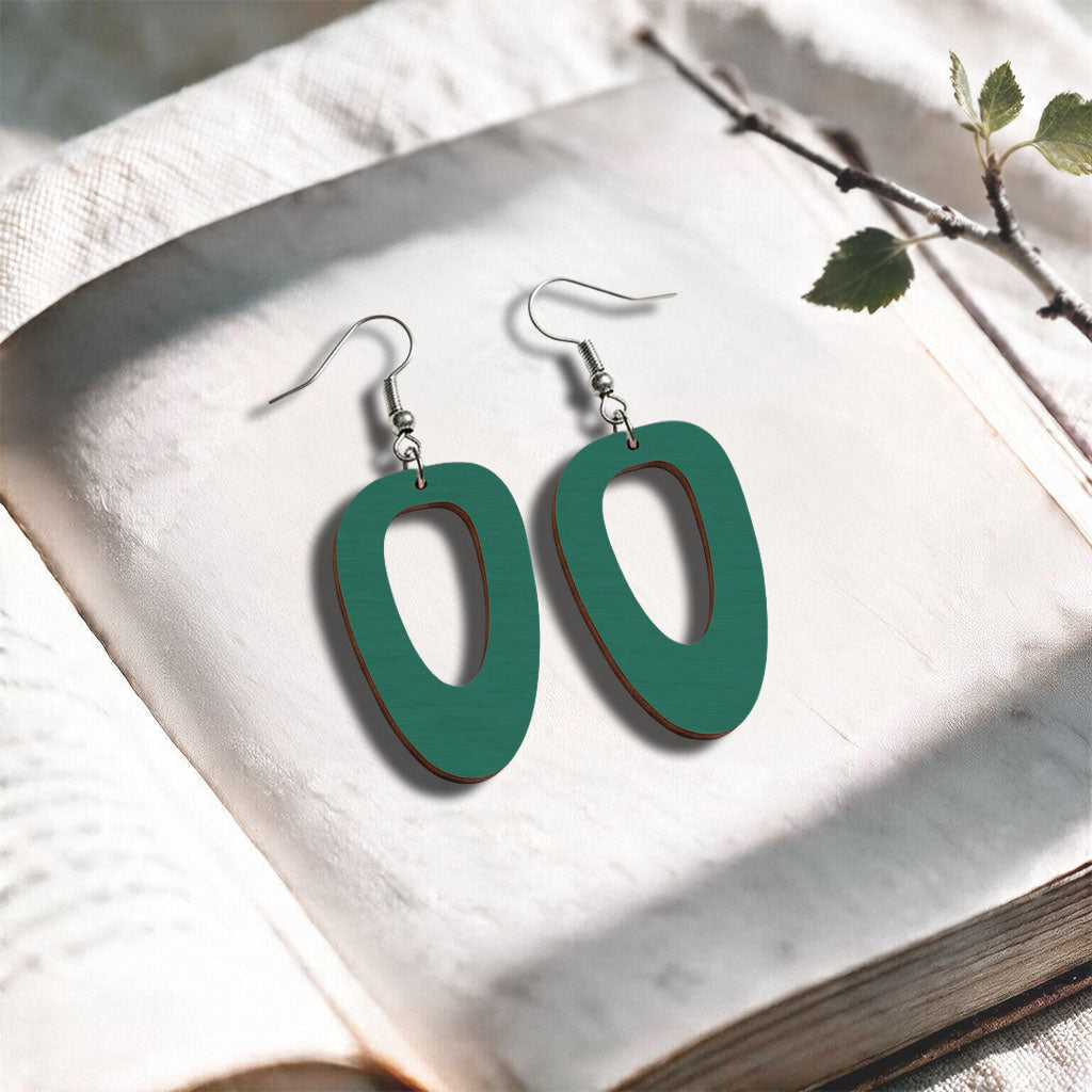Petrol Islet plywood earrings made in Finland, photographed on a vintage book in natural sunlight