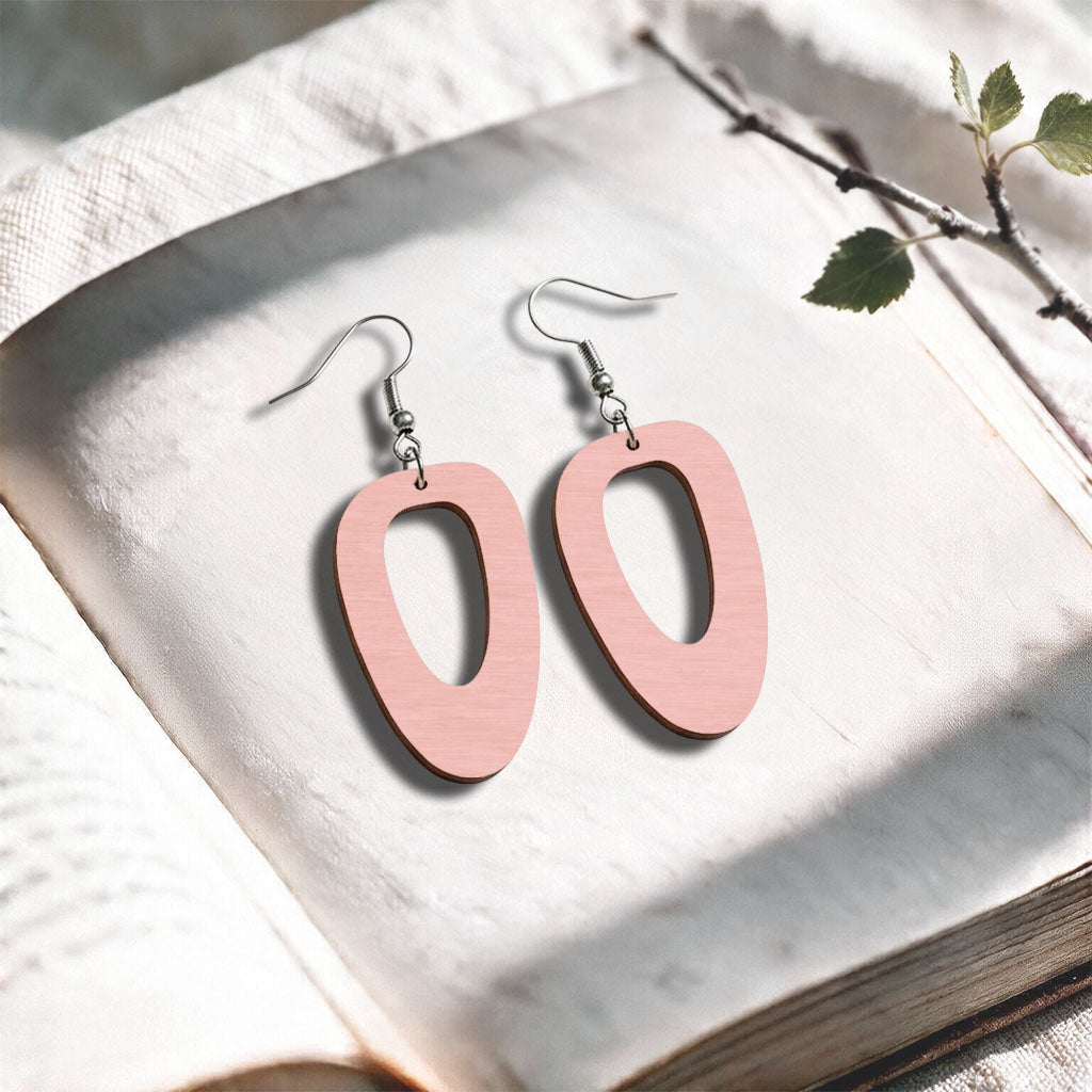 Powder Pink Islet plywood earrings made in Finland, photographed on a vintage book in natural sunlight
