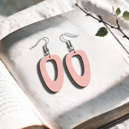 Powder Pink Islet plywood earrings made in Finland, photographed on a vintage book in natural sunlight