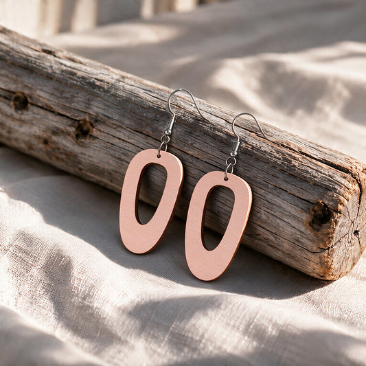 Powder Pink Islet plywood earrings made in Finland, photographed on a vintage book in natural sunlight
