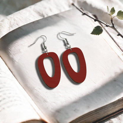 Rust red Islet plywood earrings made in Finland, photographed on a vintage book in natural sunlight