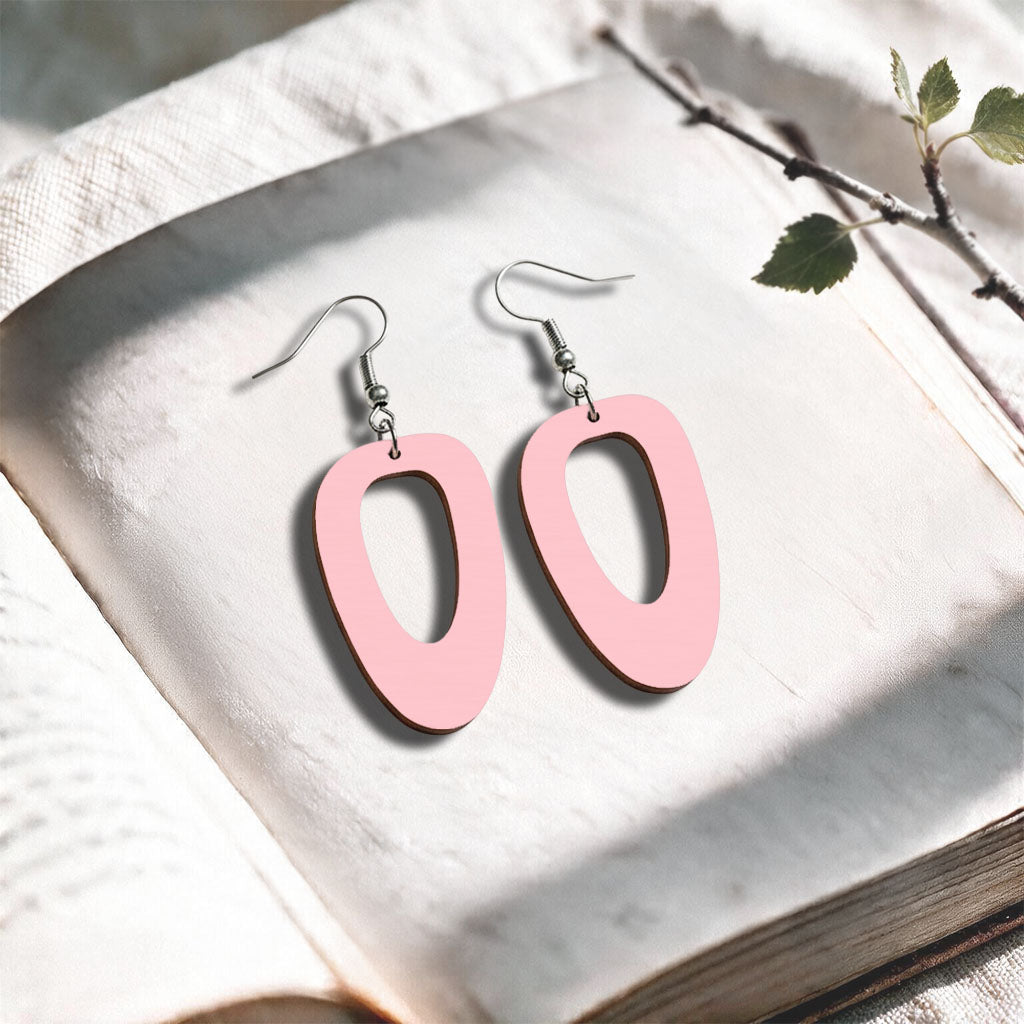 Baby Pink Islet plywood earrings made in Finland, photographed on a vintage book in natural sunlight
