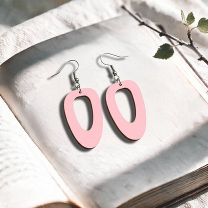 Baby Pink Islet plywood earrings made in Finland, photographed on a vintage book in natural sunlight