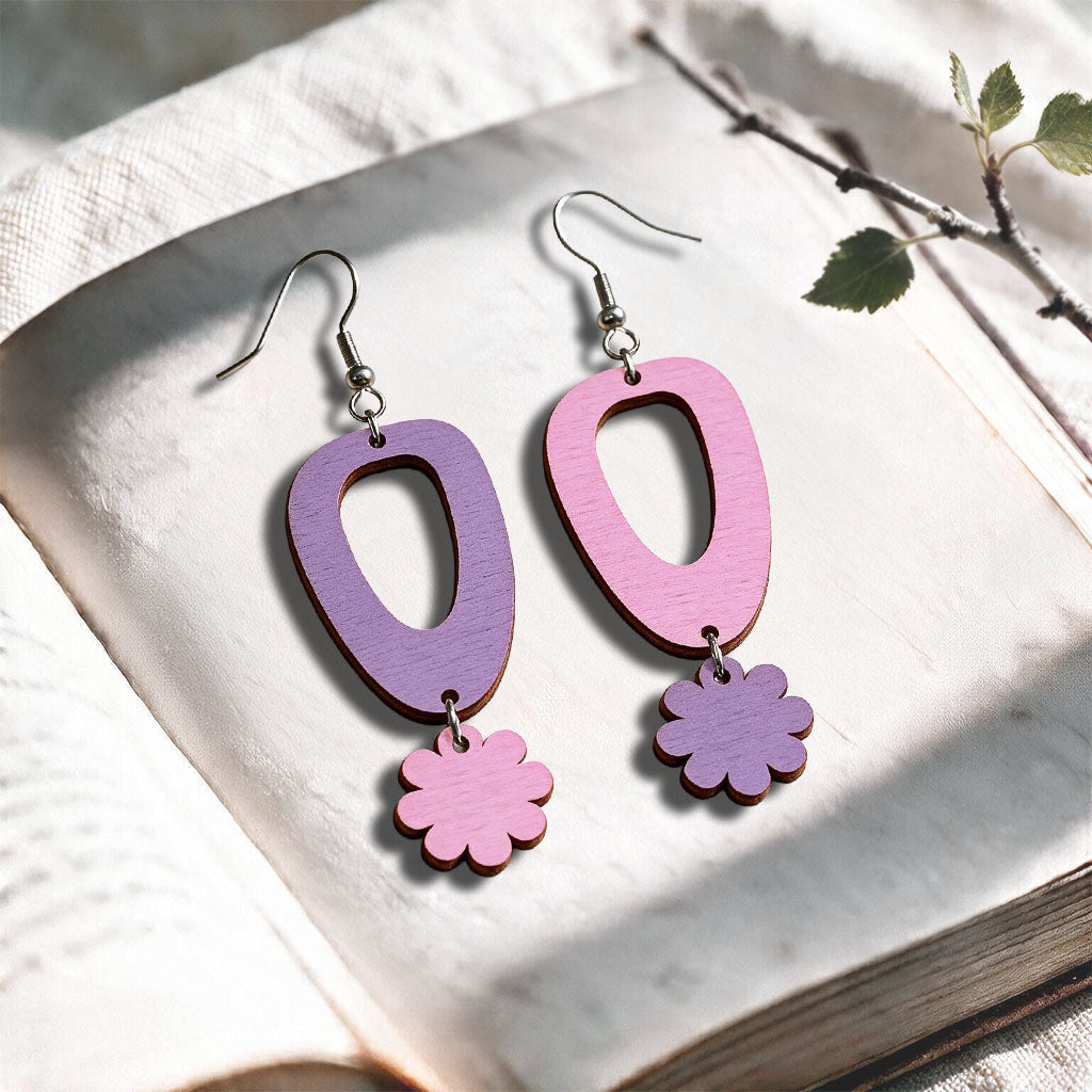 Amethyst and mauve Islet Flower plywood earrings made in Finland, photographed on a vintage book in natural sunlight