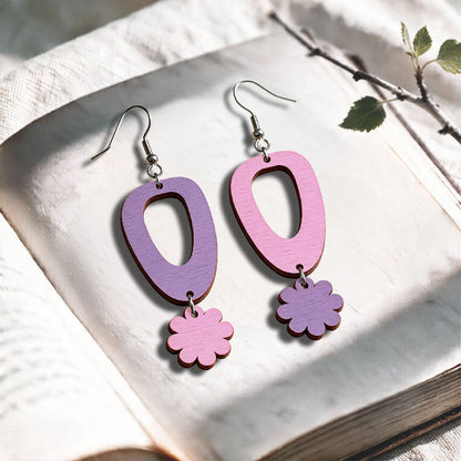 Amethyst and mauve Islet Flower plywood earrings made in Finland, photographed on a vintage book in natural sunlight