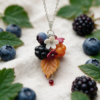 Handcrafted Finnish berry pendant featuring blueberry, blackberry and cloudberry made from polymer clay with delicate flowers and an autumn leaf. Displayed on natural linen with fresh berries and green foliage.
